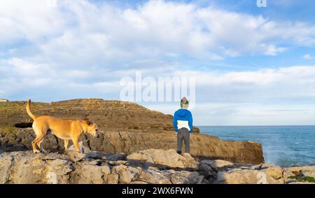 Garçon avec son chien marchant le long d'une falaise avec la mer en arrière-plan Banque D'Images