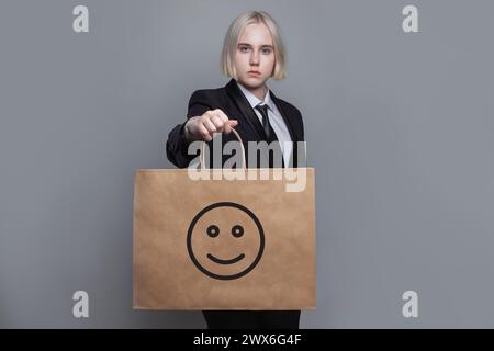 Jeune femme avec sac à provisions avec émoticône de sourire d'icône sur fond gris Banque D'Images