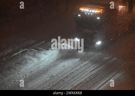 Camion roulant la nuit dans une tempête de neige, avec des feux orange sur le dessus de l'avant de la cabine du camion pour montrer le contour du camion pour la sécurité. Banque D'Images