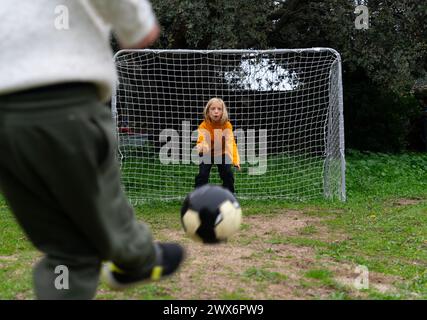 Garçon jetant un ballon de football au but et un autre gardien de but garçon attendant de l'arrêter Banque D'Images