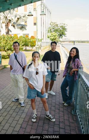 Jeunes hommes et femmes souriants en vêtements décontractés posant sur le remblai de la rivière Banque D'Images