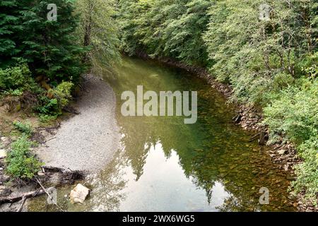Vue depuis un pont regardant en bas de la rivière avec les arbres vert lumineux reflétés dans l'eau de la rivière et un rivage rocheux. Banque D'Images