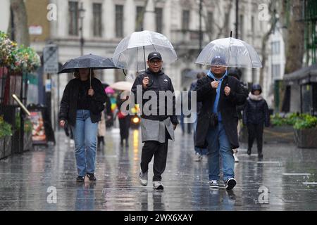 Les gens se mettent à l'abri sous des parapluies alors qu'ils marchent sous la pluie à Leicester Square à Londres. La neige est tombée dans certaines parties du sud-ouest de l'Angleterre et du pays de Galles. Les prévisionnistes disent qu'une zone de pluie, de neige gendre et de neige de colline se déplace vers le nord à travers le Royaume-Uni alors que les vacanciers se préparent à embarquer pour des escapades de Pâques. Date de la photo : jeudi 28 mars 2024. Banque D'Images