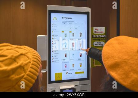 Nueva York, États-Unis - 28 mars 2024 : McDonald's où deux clientes interagissent avec un kiosque libre-service. Banque D'Images