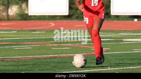 Une joueuse de soccer de lycée qui donne un coup franc au ballon de soccer pendant un match de soccer. Banque D'Images