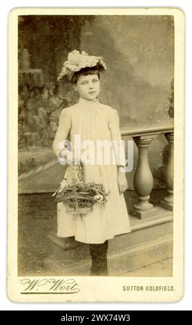 Original, charmant, victorien carte de visite (carte de visite ou CDV) de belle jeune fille victorienne, enfant victorien, lèvres de bouton de rose, âgé d'environ 6 ou 7 ans, avec frange, yeux rêveurs, portant une robe blanche, chapeau, tenant un panier de fleurs, studio de W. Wort, Ashby House, Sutton Coldfield, Warwickshire (maintenant Birmingham) Royaume-Uni vers 1885. Banque D'Images