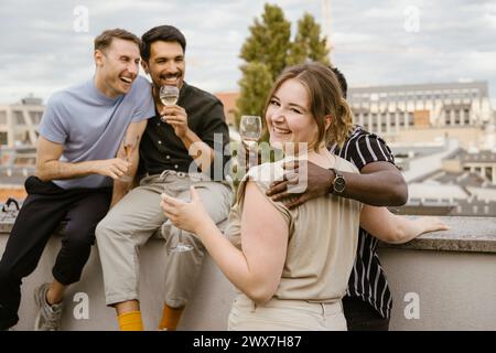 Portrait de femme souriante regardant par-dessus l'épaule tout en profitant de boissons avec des amis masculins sur le pont sur le toit Banque D'Images