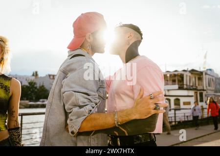 Vue latérale d'un homme gay romantique embrassant un ami non binaire sur la promenade Banque D'Images