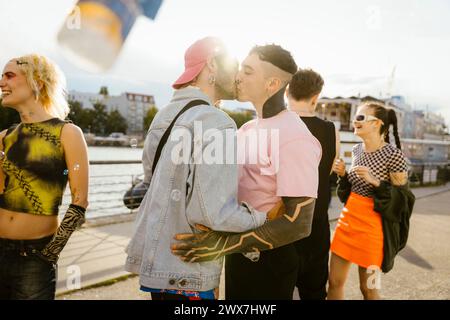 Homme gay affectueux embrassant une personne non binaire sur la promenade en ville Banque D'Images