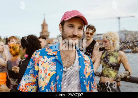 Portrait d'homme gay souriant portant une chemise florale avec des amis non binaires appréciant en arrière-plan Banque D'Images