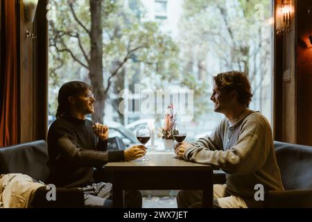 Couple gay souriant prenant du vin tout en étant assis à table dans le restaurant Banque D'Images