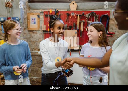 Étudiante souriante faisant une poignée de main avec un professeur lors d'un atelier technologique à l'école Banque D'Images