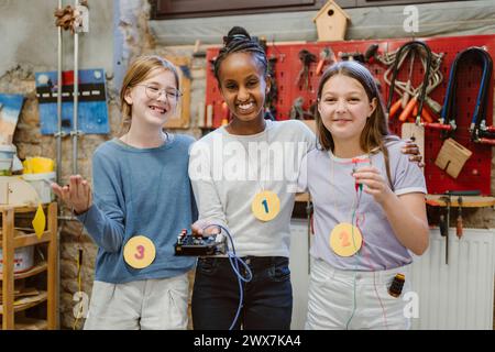 Portrait d'étudiantes heureuses montrant des pièces électriques lors d'un atelier technologique à l'école Banque D'Images