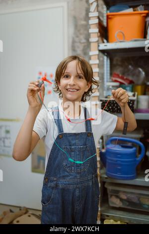 Portrait d'une étudiante souriante tenant un moteur électrique connecté à des fils à l'atelier de technologie à l'école Banque D'Images