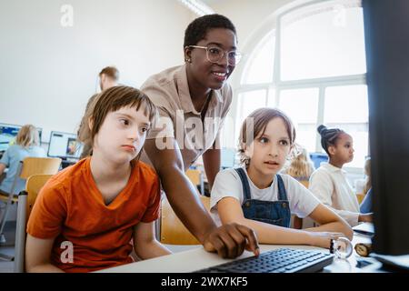 Enseignante souriante aidant une fille trisomique 21 en classe d'informatique à l'école Banque D'Images