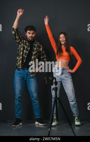 Beau jeune couple souriant tirant des mouvements de danse sur la caméra de smartphone sur fond noir. Vidéo populaire de contenu musical tendance pour les médias sociaux Banque D'Images