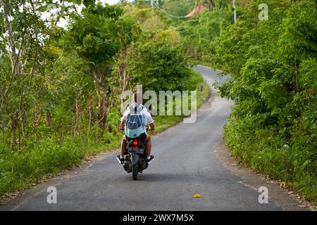 Une personne sur une moto emprunte une route asphaltée pittoresque en Asie. Bali, Indonésie - 12.30.2022 Banque D'Images