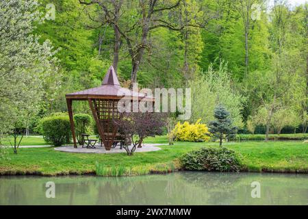 La belle vue sur le parc avec les arbres, terrain d'herbe verte, gazebo et l'étang sur le fond de ciel bleu et de nuages blancs, printemps Banque D'Images