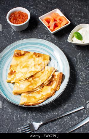 Fines crêpes russes ou blini avec caviar rouge et saumon sur table noire. Banque D'Images