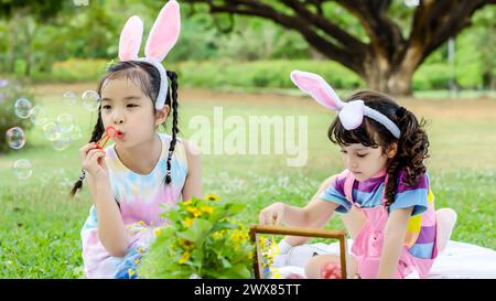 Deux jeunes filles portant des oreilles de lapin soufflent des bulles de savon lors d'un événement en plein air Banque D'Images