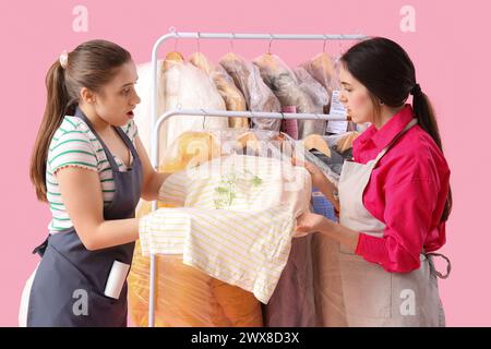 Ouvrières féminines de nettoyeur à sec avec des vêtements tachés sur fond rose Banque D'Images