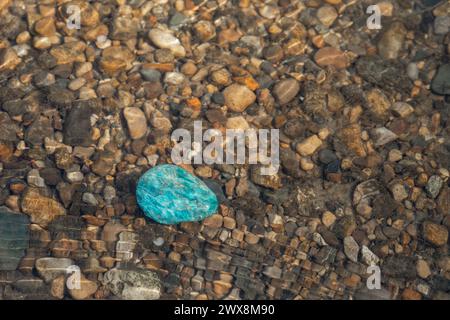 Une pierre précieuse d'apatite polie dans l'eau peu profonde sur de petites pierres dans un ruisseau Banque D'Images
