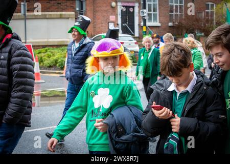 Garçon portant un chapeau violet avec des cheveux jaunes regarde son ami au téléphone dans la parade de la St Patrick de Warrington en 2024 Banque D'Images