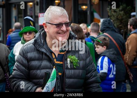 Un mâle aux cheveux argentés rit pendant la parade de la St Patrick de Warrington en 2024 Banque D'Images