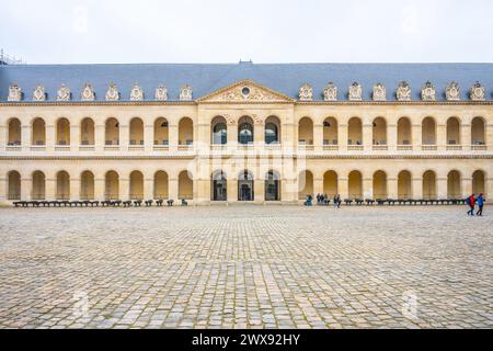 Les visiteurs traversent la cour pavée des Invalides sous un ciel couvert de Paris, France Banque D'Images