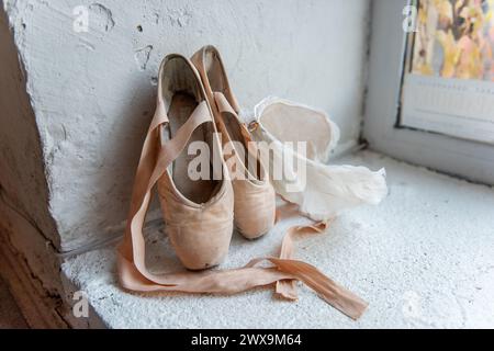 Chaussures pointe bien utilisées avec des rubans, tiadre de plume blanche se trouvent à côté de la fenêtre, racontant l'histoire du dévouement et l'art gracieux du ballet. Banque D'Images