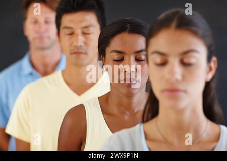 Diversité, personnes et rangée avec les yeux fermés pour la méditation dans un fond sombre pour la paix, le calme et l'esprit sain. Groupe, debout et concentration au yoga Banque D'Images