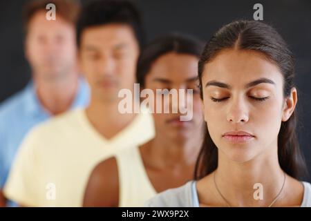 Diversité, les gens et la rangée avec les yeux fermés pour méditer dans un fond sombre pour la paix, le calme et l'esprit sain. Groupe, debout et concentré pour le yoga Banque D'Images