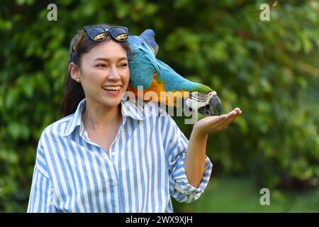 Femme heureuse nourrissant l'aras bleu et jaune (Ara ararauna) oiseau sur sa main Banque D'Images