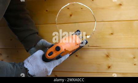 travailler avec une scie sauteuse sur une surface en bois, couper un cercle avec une scie sauteuse, un outil de construction de travail dans les mains masculines dans des gants en gros plan pendant le travail Banque D'Images