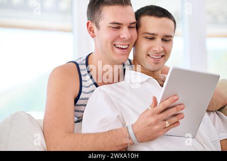 Tablette, sourire et couple gay sur canapé pour la vidéo, le film ou google IT, inscrivez-vous ou service de streaming à la maison. LGBTQ, l'amour et les gens s'embrassent dans le salon Banque D'Images