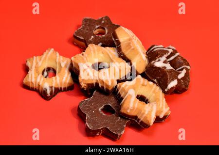Biscuits sablés avec et sans chocolat se trouvent en tas sur un fond rouge, gros plan. Banque D'Images