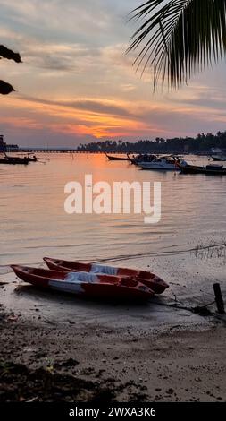 Un bateau rouge et blanc éclatant repose paisiblement sur la plage de sable, ses couleurs contrastant avec la mer bleue et le rivage doré. Koh Libong Thaïlande Banque D'Images