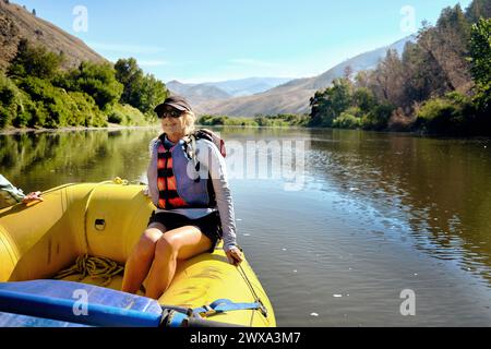 Femme senior souriante assise sur le radeau gonflable flottant sur la rivière Banque D'Images