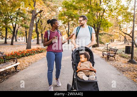 Couple de races mixtes promène la poussette de leur fils à travers le parc Banque D'Images