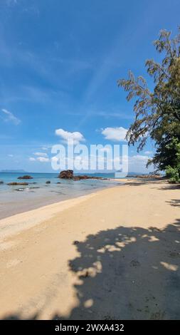 Une plage de sable tranquille rencontre le vaste océan sous un ciel bleu clair, créant un cadre pittoresque où les vagues embrassent doucement le rivage.Koh Libong Thaïlande Banque D'Images