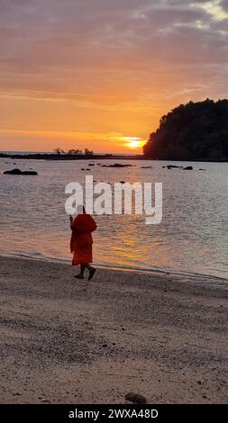 Un moine thaïlandais solitaire se promène le long de la plage de sable au coucher du soleil, créant une silhouette fascinante sur le ciel coloré. Koh Libong Thaïlande Banque D'Images