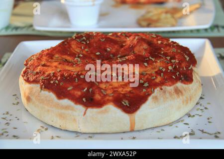 Un calzone avec sauce tomate et herbes sur le dessus sur une assiette. Banque D'Images
