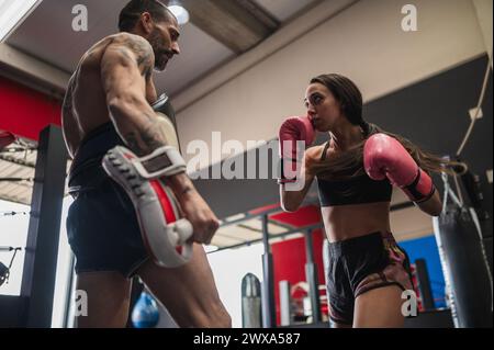 Forte boxeur féminin sparring avec entraîneur personnel pendant l'entraînement Banque D'Images