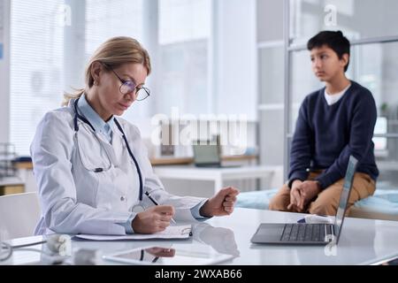 Portrait de femme médecin portant des lunettes prenant des notes avec l'enfant assis sur le lit dans l'espace de copie de fond Banque D'Images