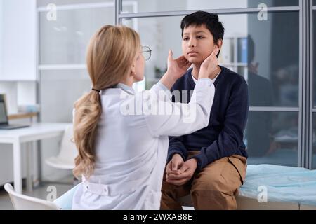 Vue arrière d'une femme médecin examinant le cou et la gorge d'un jeune garçon lors d'un bilan de santé en clinique pédiatrique Banque D'Images