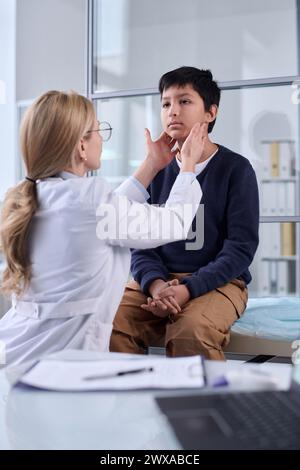 Portrait vertical d'un pédiatre examinant le cou et la gorge d'un jeune garçon lors d'un bilan de santé en clinique Banque D'Images