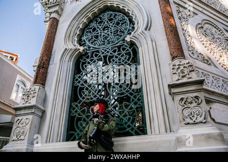 Une personne avec un foulard rouge regardant à travers une fenêtre gothique complexe sur une façade décorative en pierre Banque D'Images