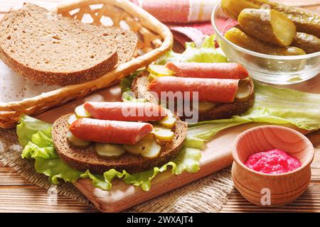 Sandwichs faits maison avec saucisses fumées tranchées et conserves de cornichons. L'apéritif froid avec pain foncé et sauce au raifort épicée. Banque D'Images