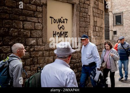 Alors que la semaine Sainte se déroule dans le quartier gothique de Barcelone, les visiteurs passent devant un graffiti contre le tourisme Reading Tourist rentrent chez eux. Manifestations contre le tourisme de masse h Banque D'Images