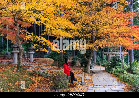 Femme asiatique assise près de 2 érables jaunes vibrants dans le jardin du temple Enkoji, Kyoto. Banque D'Images